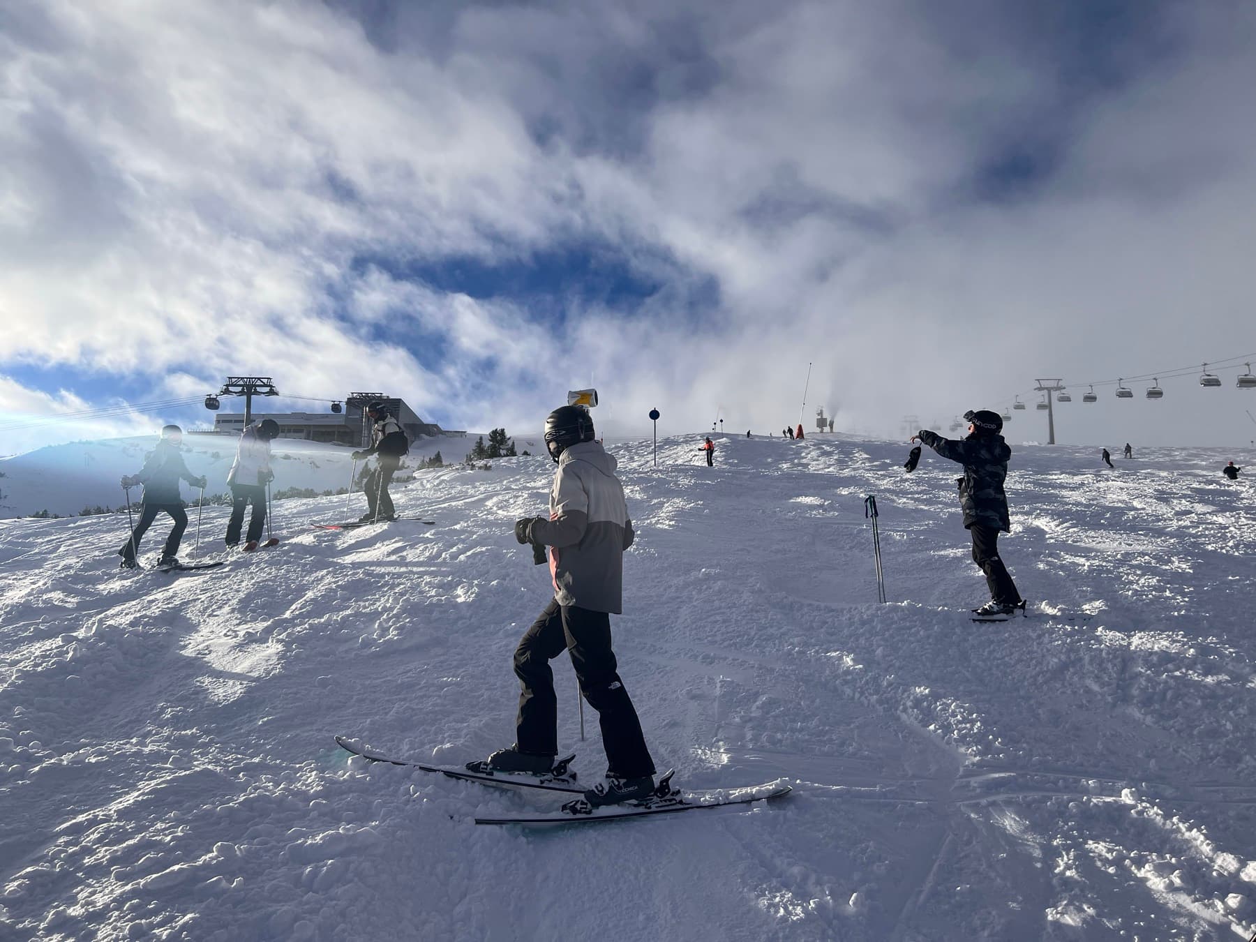 Skiers at the top of a piste under a bank of cloud, lifts running behind them