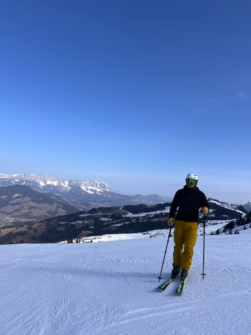 A skier stopped on a groomed piste with jagged peaks on the horizon