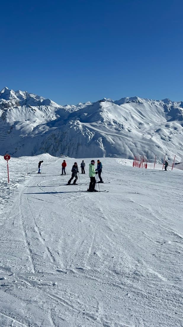 A wide empty piste on a bluebird day with mountains behind