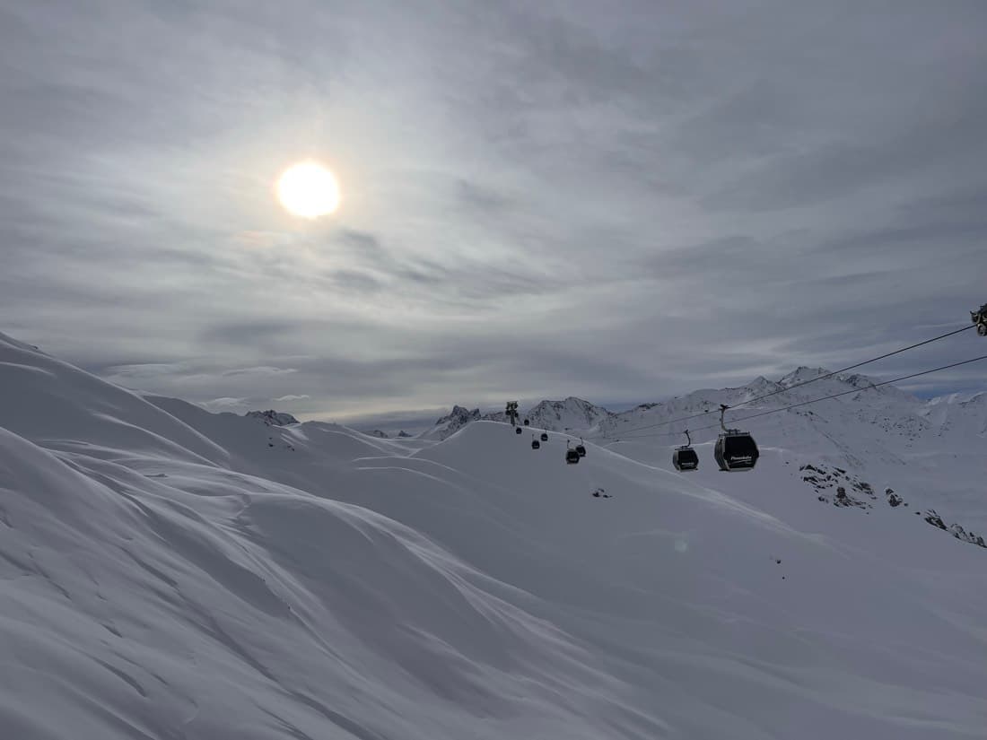 Gondolas crossing a snowfield with the sun breaking through cloud