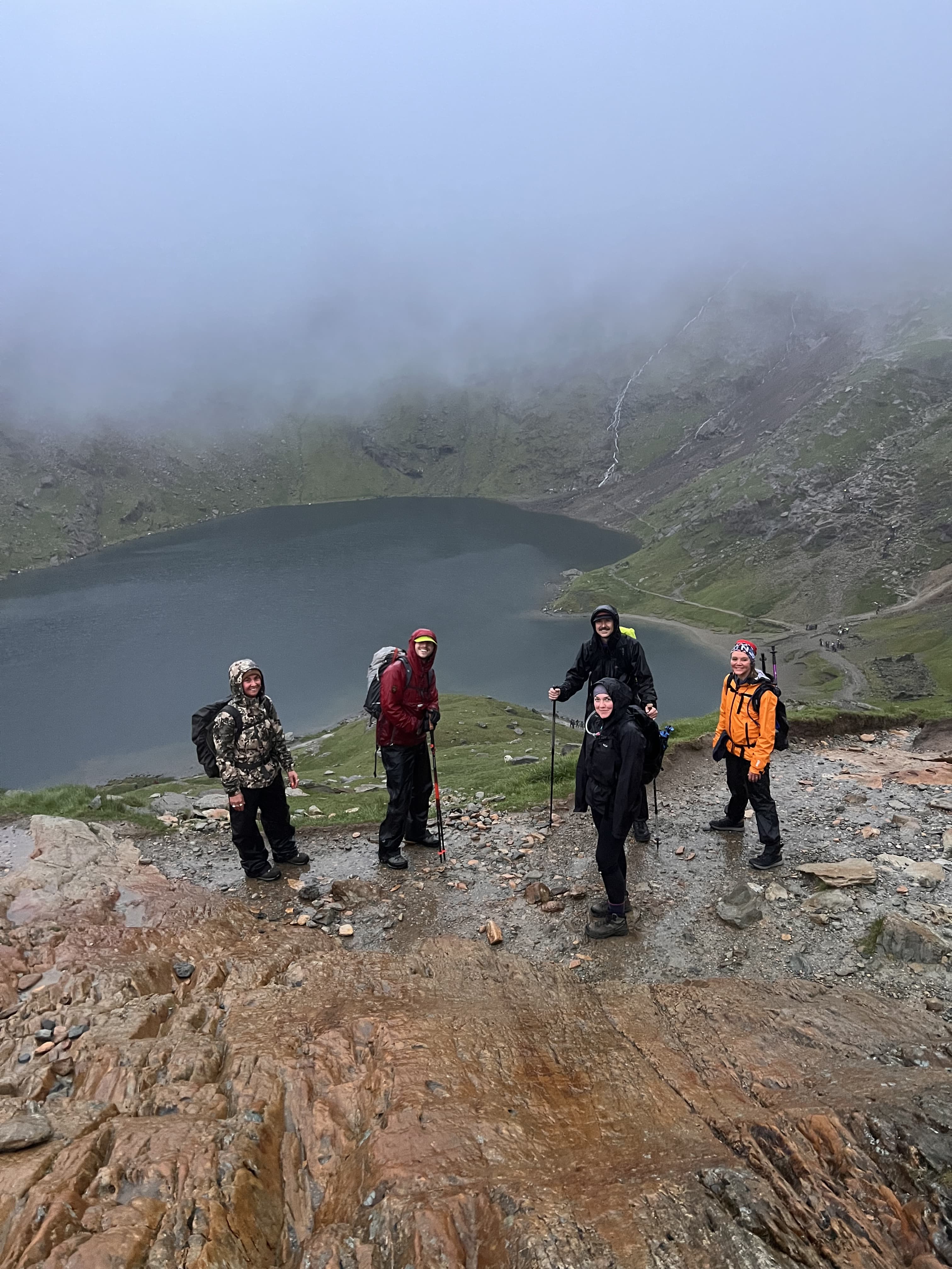 Six walkers in waterproofs on a wet rocky path above Llyn Llydaw in low cloud, Snowdonia